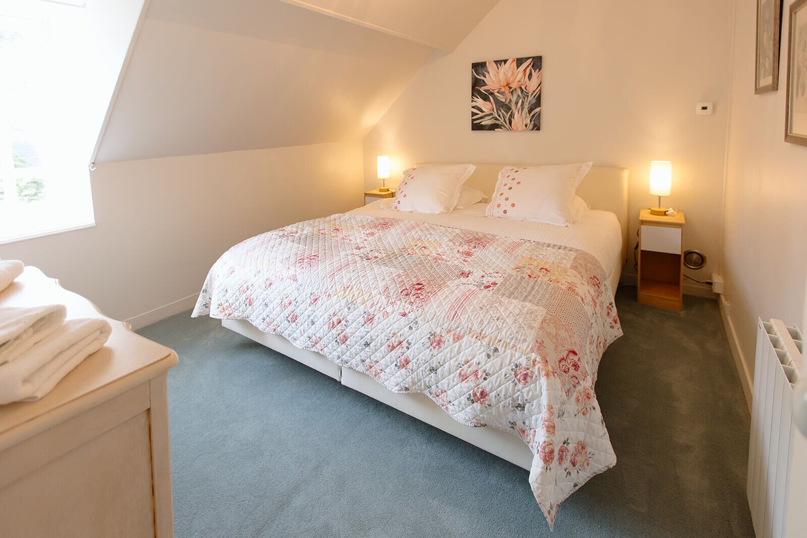 A bedroom with a bed, two bedside tables, a radiator, and a window.