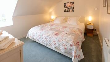 A bedroom with a bed, two bedside tables, a radiator, and a window.