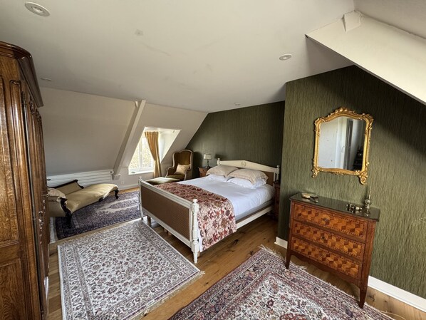 A bedroom with a sloped ceiling, a bed with a floral bedspread, a wooden dresser, a mirror, and a chair.