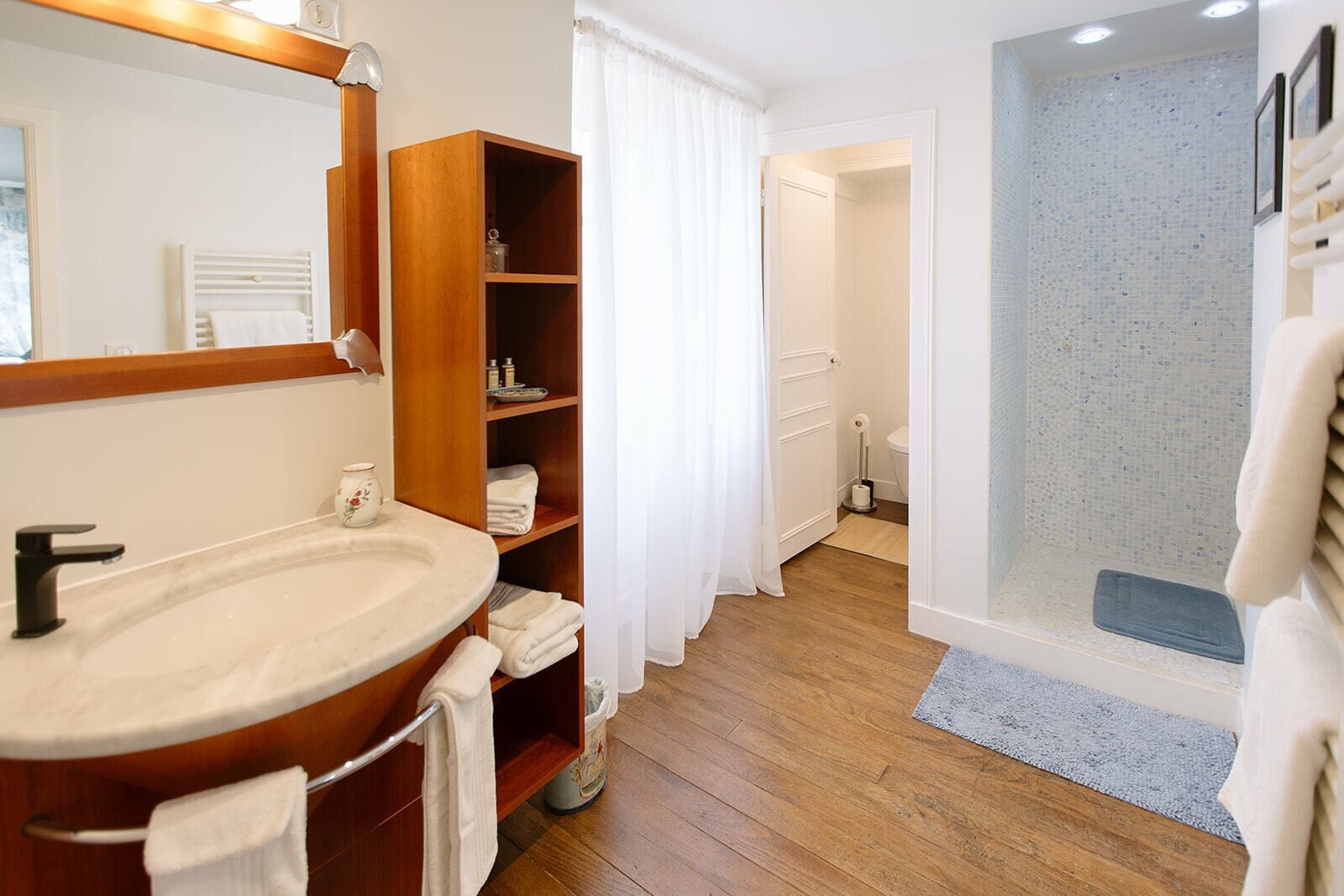 A bathroom with a wooden vanity, a sink, a mirror, a shower with a glass door, and a toilet visible through a door.