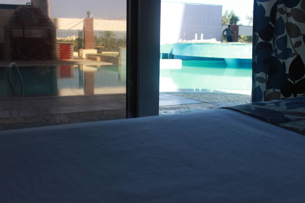 A view of a swimming pool from a window, with a clear sky and a building in the background.