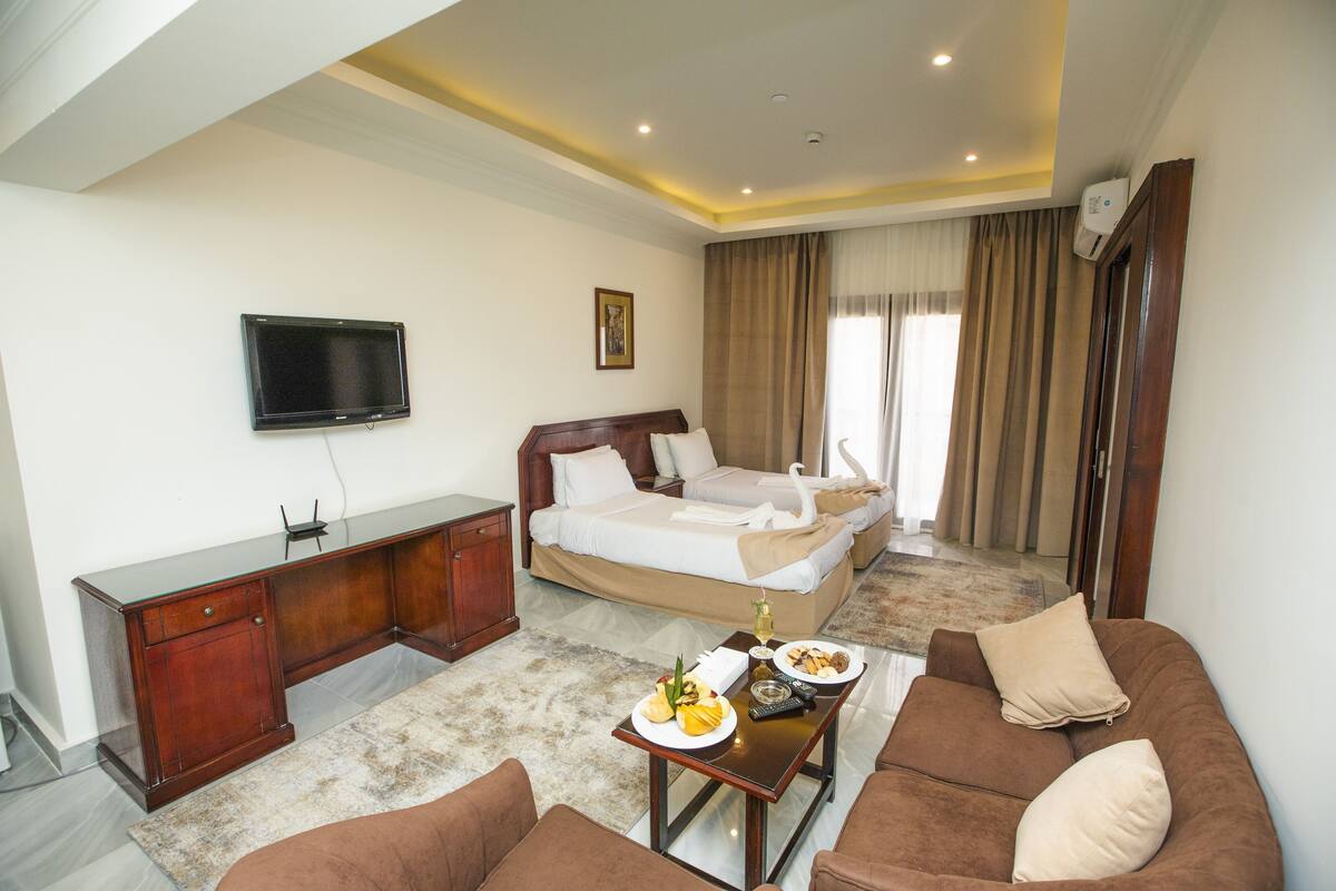 A hotel room with a bed, a TV, a desk, a sofa, and a dining table with food.
