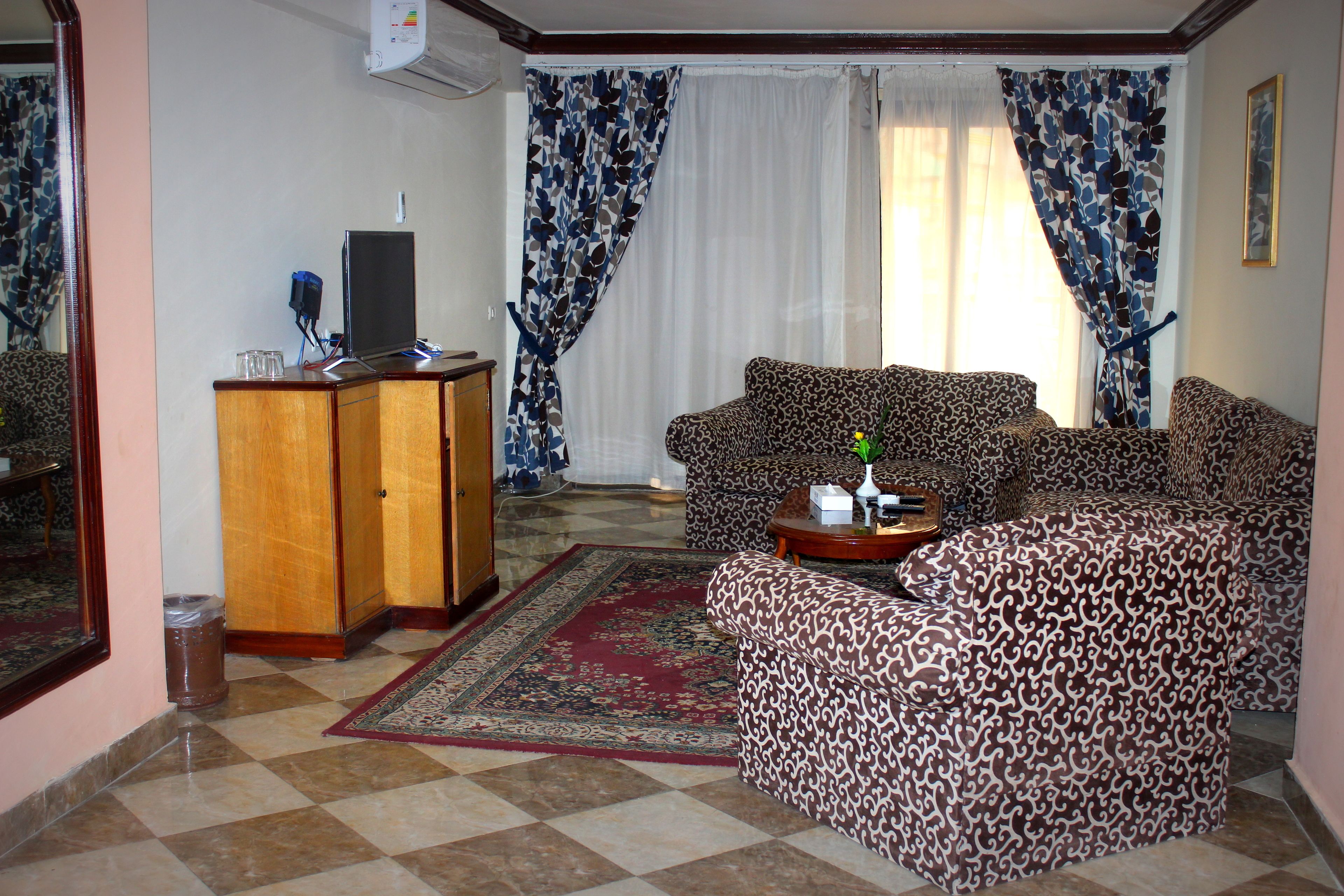 A living room with patterned sofas, a wooden cabinet, and a red rug.