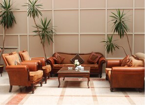 A living room with a brown leather sofa set, matching armchairs, a glass coffee table, and two potted plants. - Aifu Resort (Alexandria)
