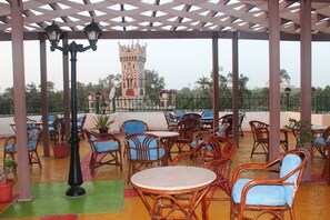 A covered outdoor seating area with wicker chairs and tables, a decorative lamp post, and a view of a distant tower. - Aifu Resort (Alexandria)
