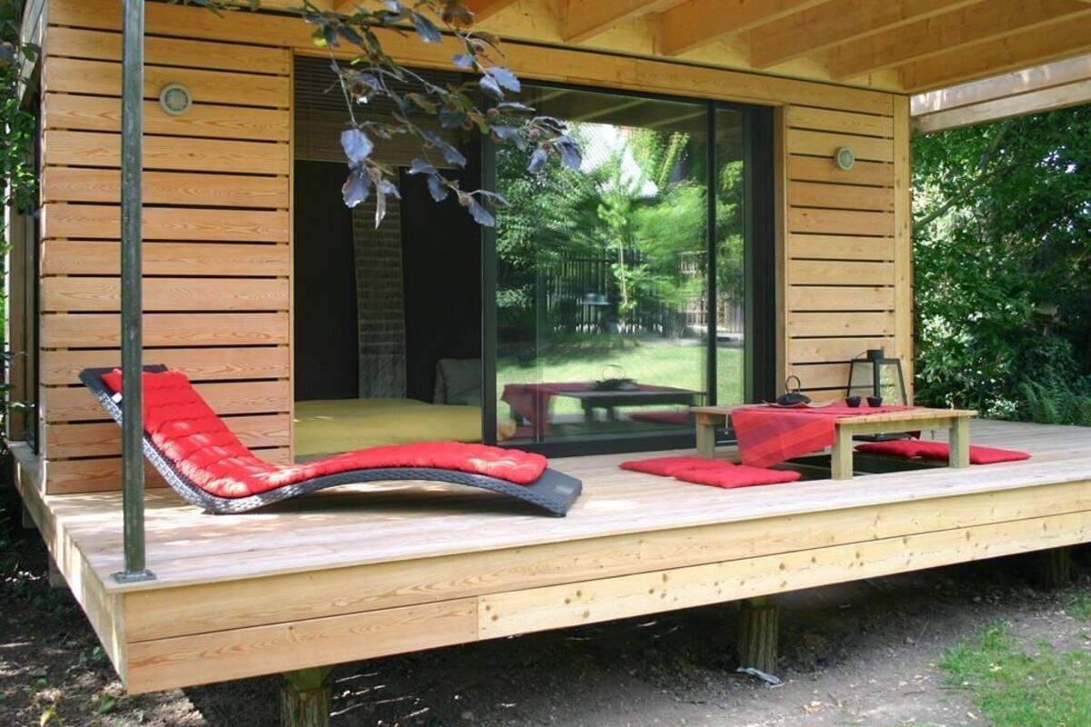 Une terrasse en bois avec un fauteuil de relaxation rouge doté d’un coussin et une petite table.