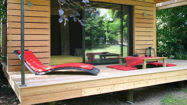 A wooden deck with a red cushioned lounge chair and a small table. - Lescalier (Brumath)