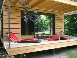 Una terraza de madera con una sillona roja acolchada y una mesita.