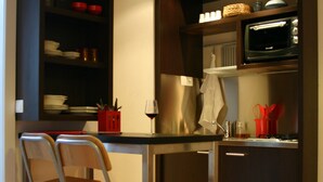 A compact kitchen with a wooden floor, a dining table, two foldable chairs, a microwave, and a small cabinet. - Lescalier (Brumath)