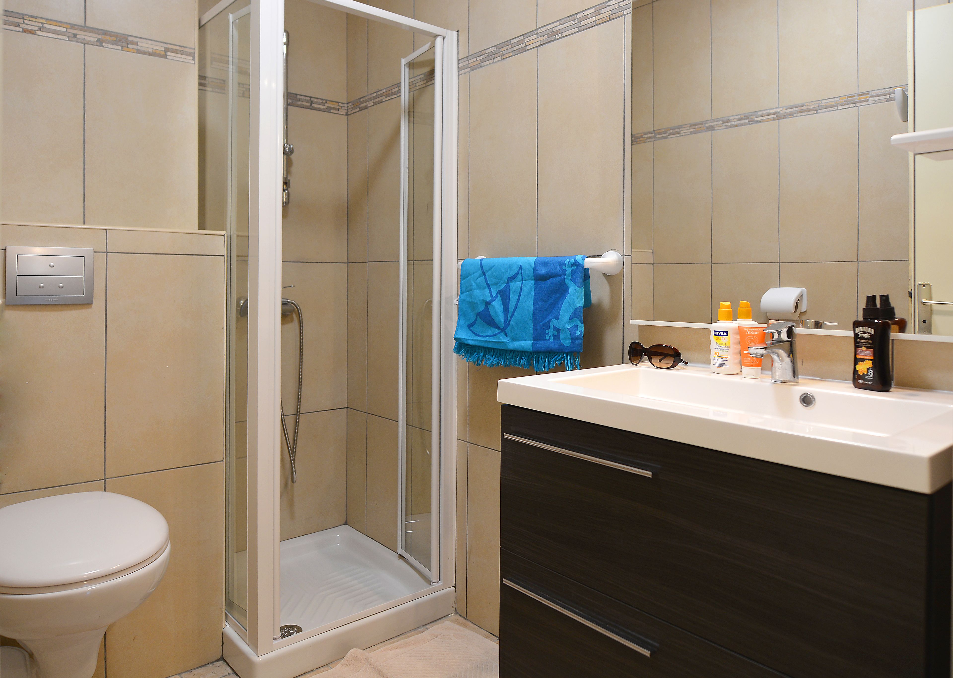 A bathroom with a glass-enclosed shower, a white toilet, a dark wooden cabinet, and a sink with toiletries.