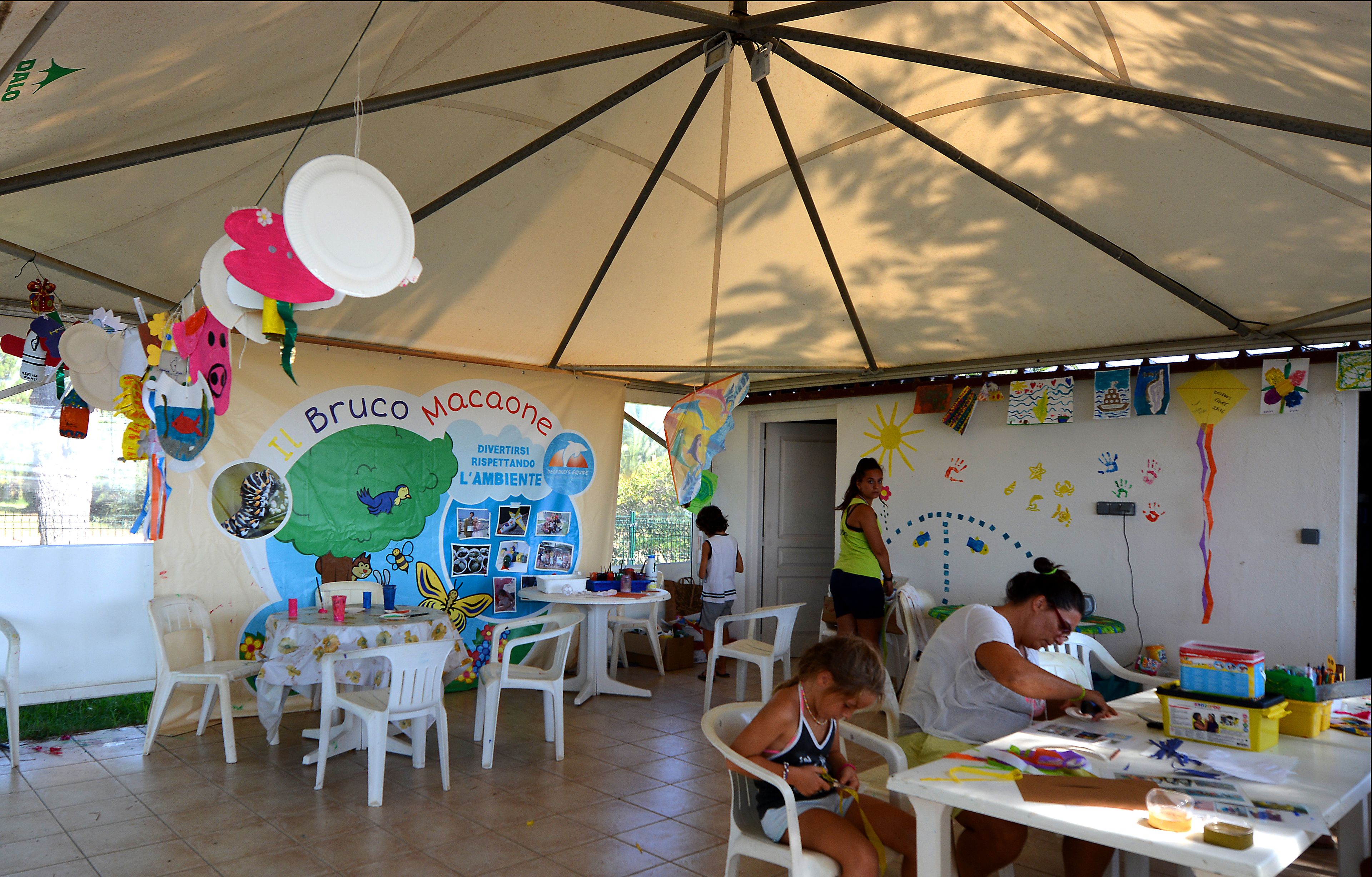 Una festa per bambini sotto una grande tenda, con tavoli e sedie, decorata con oggetti colorati e disegni sui muri.