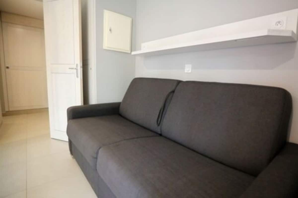 Un canapé gris dans une pièce avec une porte blanche et une étagère blanche au mur.