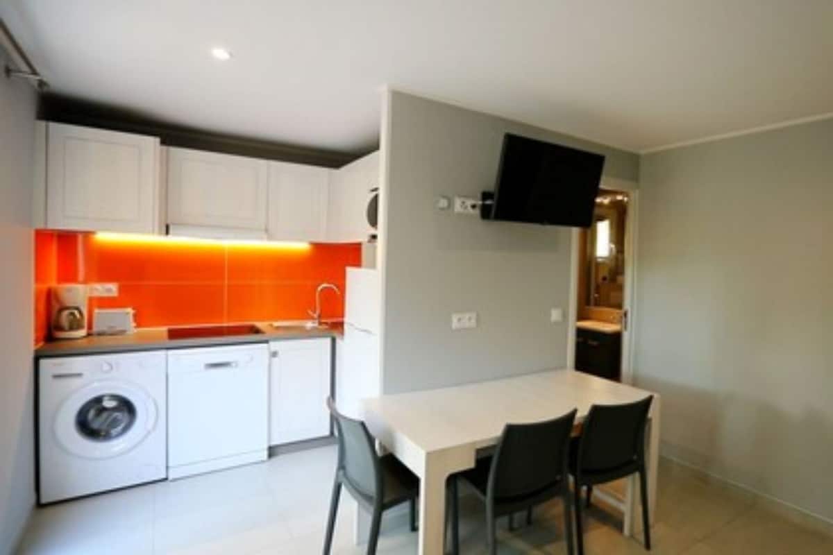Une cuisine compacte équipée d’un lave-linge, d’une table à manger avec des chaises et d’un téléviseur à écran plat fixé au mur.