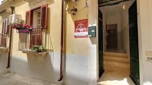 A building with a ground-floor entrance, a small balcony with potted plants, and a sign above the door. - B&B del Carmine (Noto)