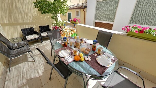 A dining area with a round table set for four, surrounded by chairs. There is a small table with a plant and flowers on the balcony. - B&B del Carmine (Noto)