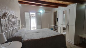 A bedroom with a bed, a white chair, a wardrobe, and a balcony with a view. - B&B del Carmine (Noto)