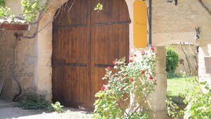 A rustic stone building with a large wooden door, a hanging lantern, and a sign that reads "Acuiel". - La Mandarine (Piolenc)