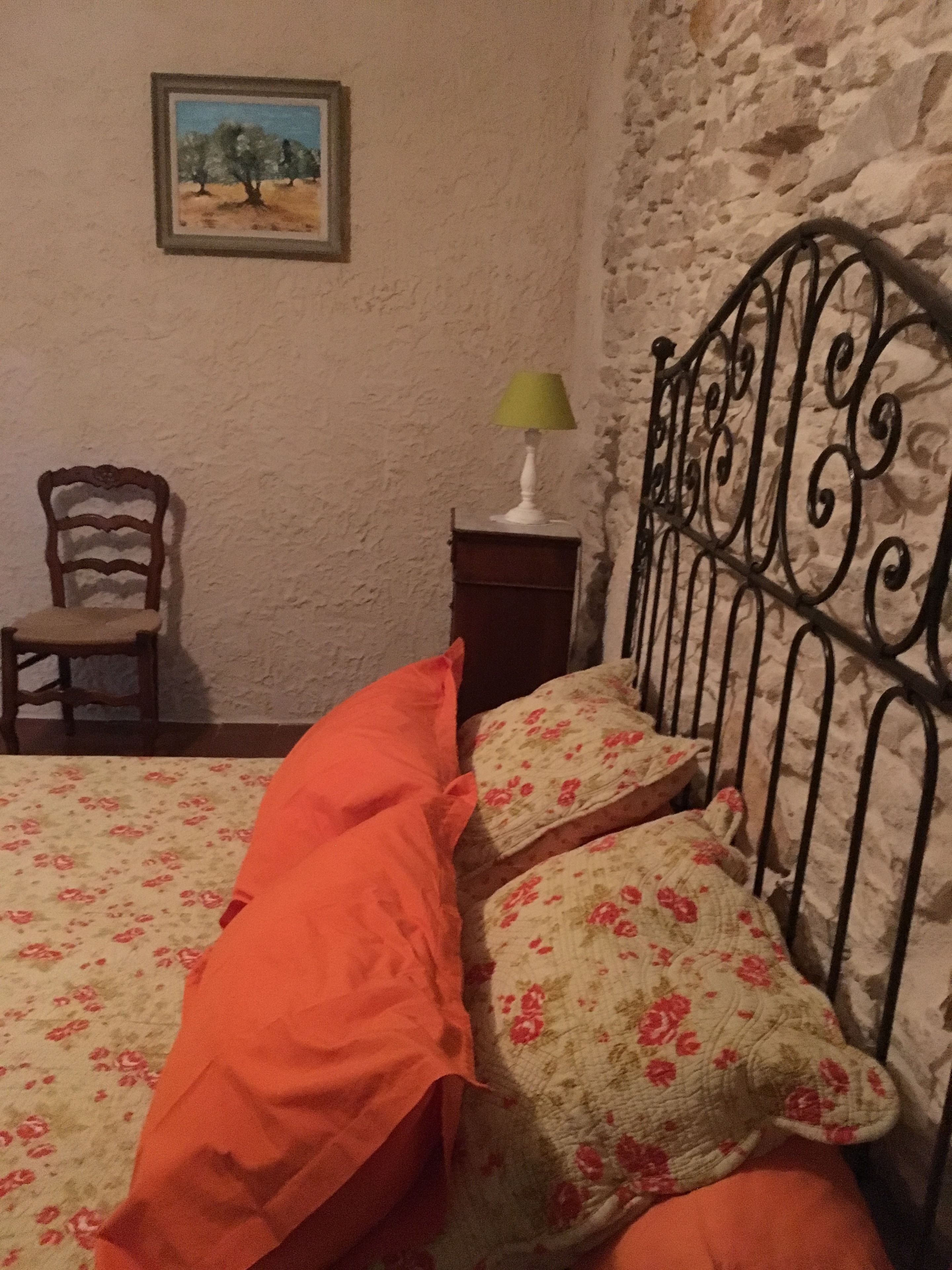 A bedroom with a bed, a chair, a nightstand, a lamp, and a painting on the wall.