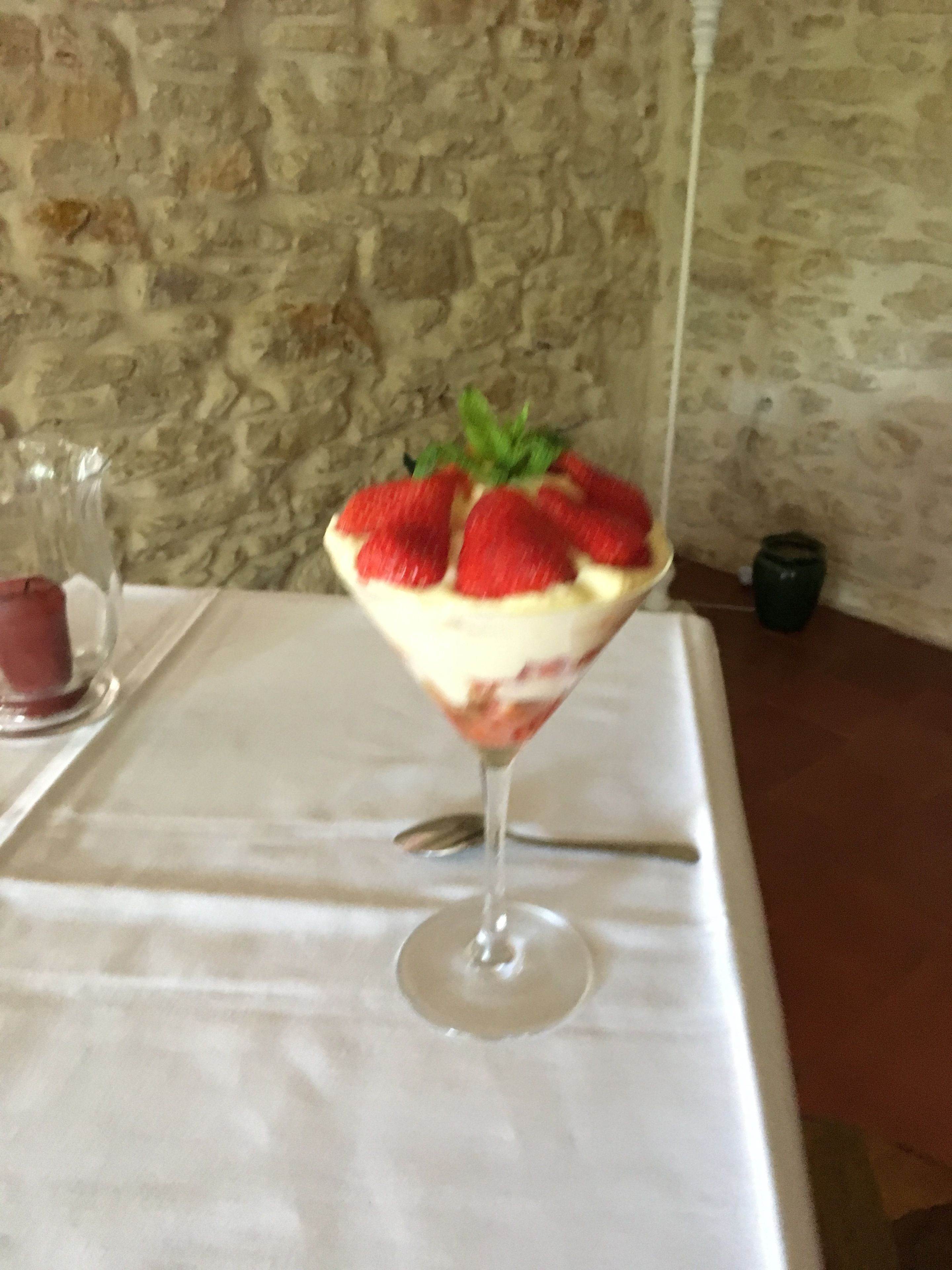 A dessert in a glass on a table with a stone wall in the background.