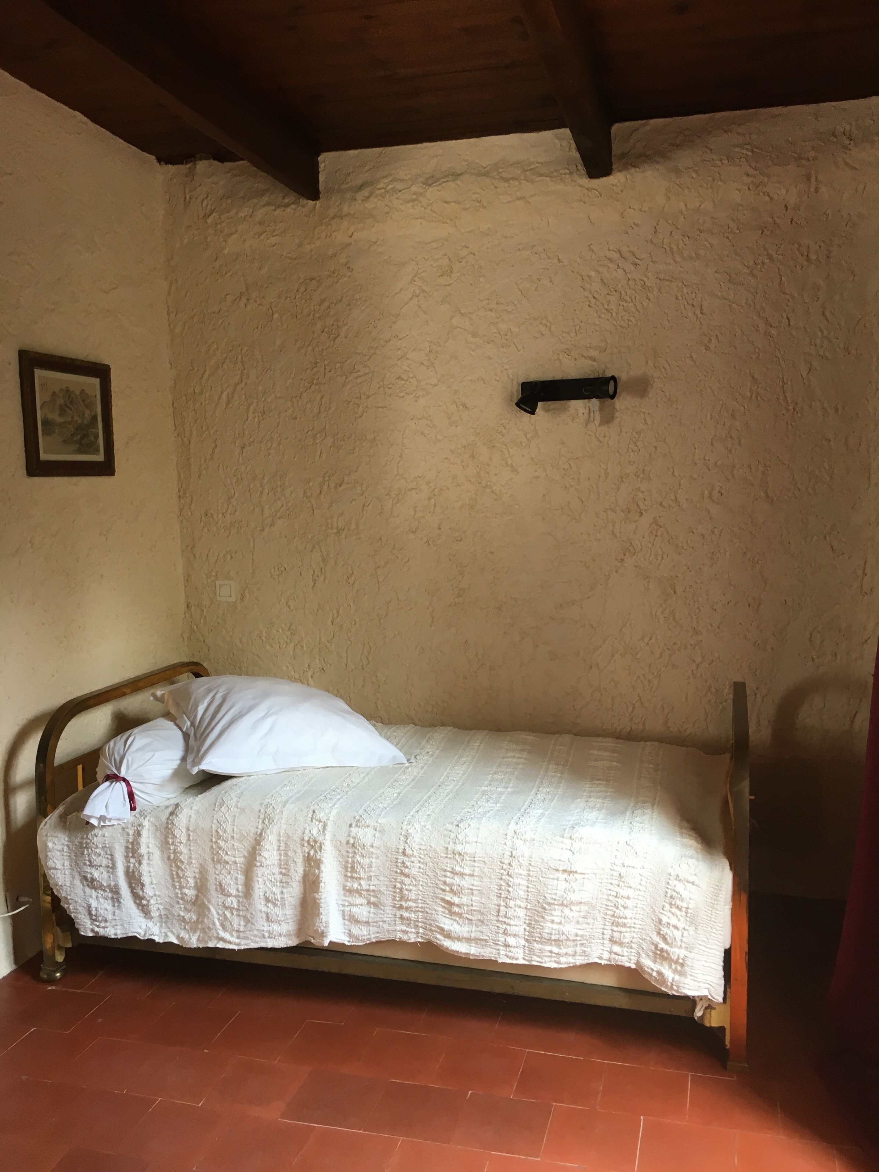 A single bed with white bedding in a room with a textured beige wall and a wooden ceiling.