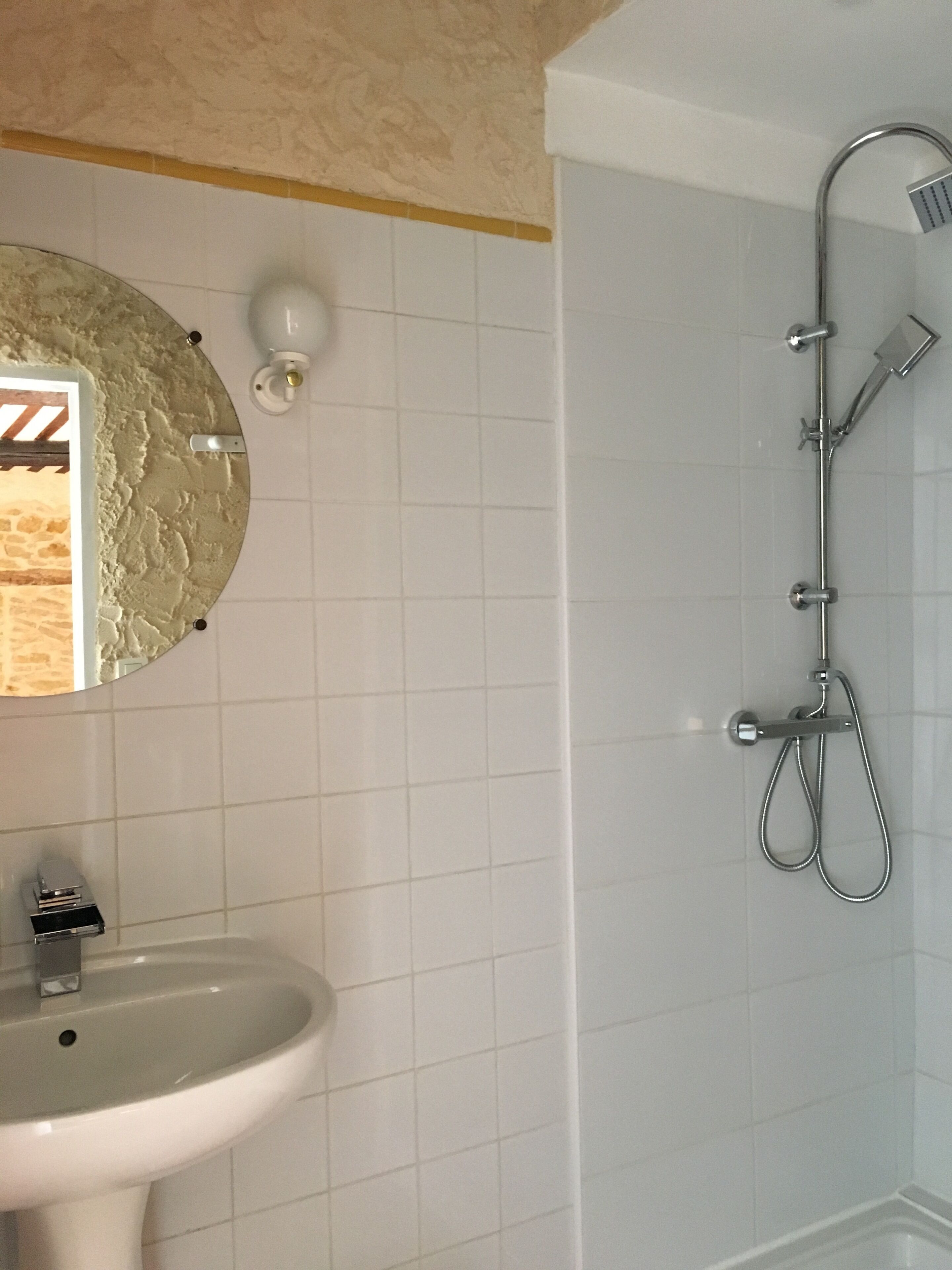 Un baño con un lavamanos blanco, un espejo y una ducha con cabezal de ducha de mano.