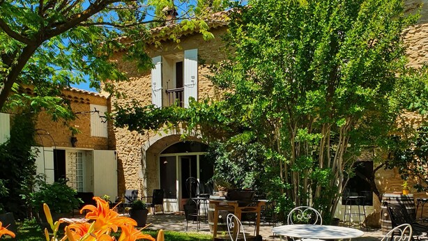 A courtyard with a stone building, outdoor seating, and orange lilies. - La Mandarine (Piolenc)