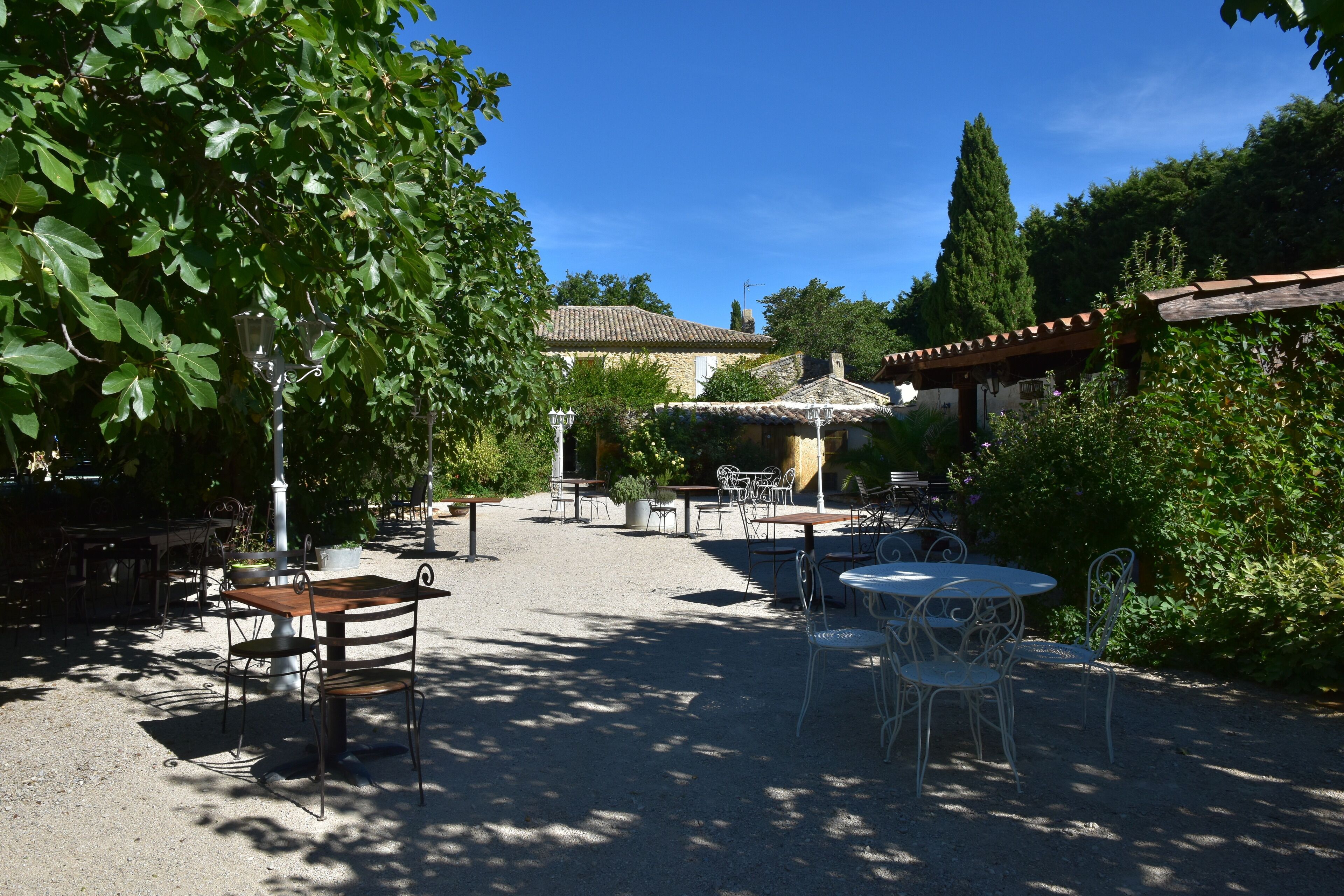 Eine Terrassenanlage im Freien mit Tischen und Stühlen, umgeben von Pflanzen und einem Gebäude mit einem Ziegeldach.
