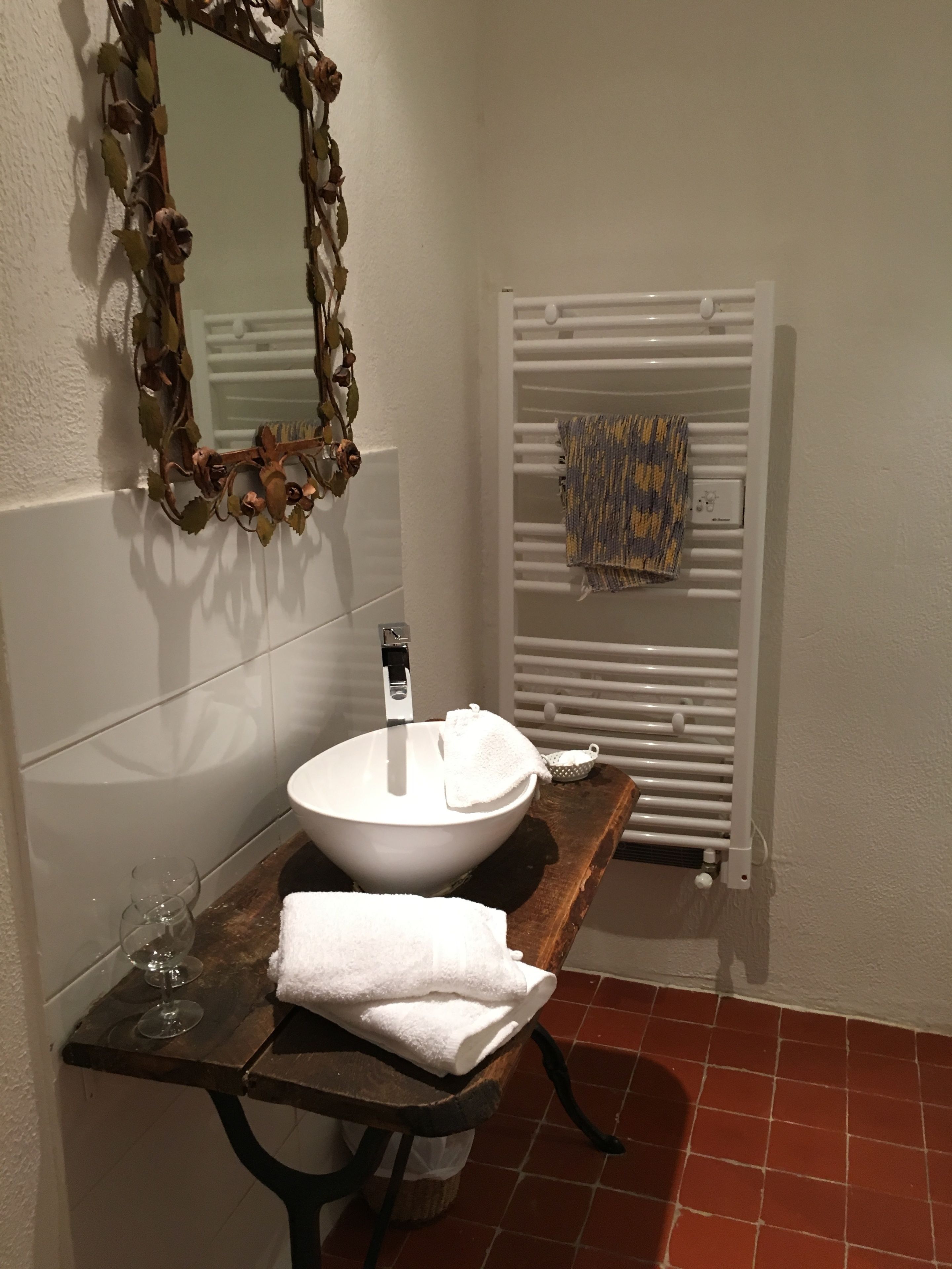 Uma casa de banho com uma pia branca, um espelho com moldura decorativa, um porta-toalhas com toalha e um radiador.
