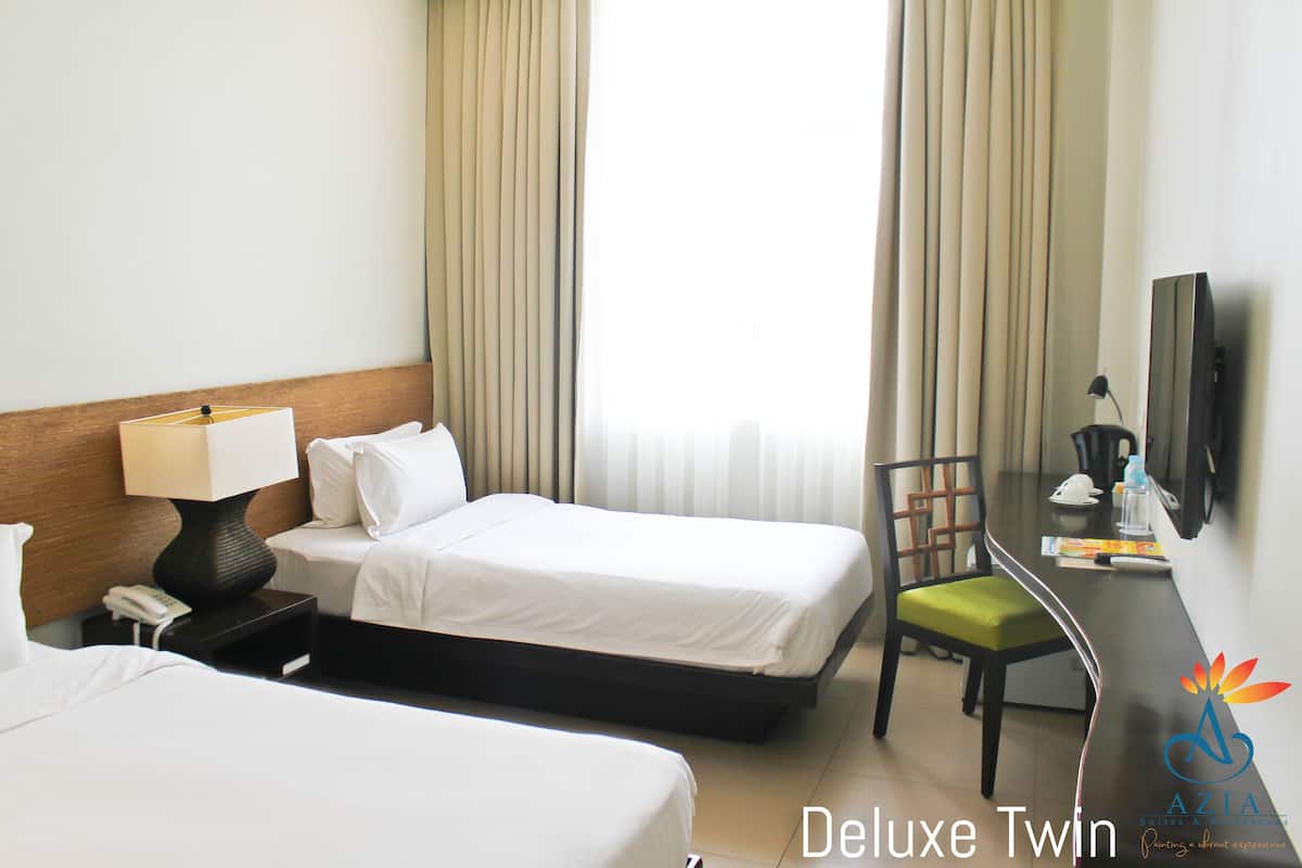 Une chambre d’hôtel avec deux lits, un bureau avec une chaise, un téléphone et une télévision.