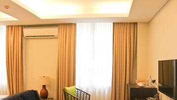 A hotel room with a bed, a desk with a lamp, a television, and an air conditioning unit.