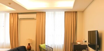 Habitación de hotel con cama, escritorio con lámpara, televisor y aire acondicionado.