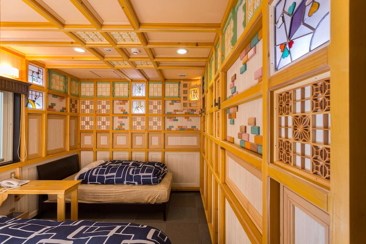 A room with two beds, a desk, and a phone. The walls have decorative panels and windows with stained glass.