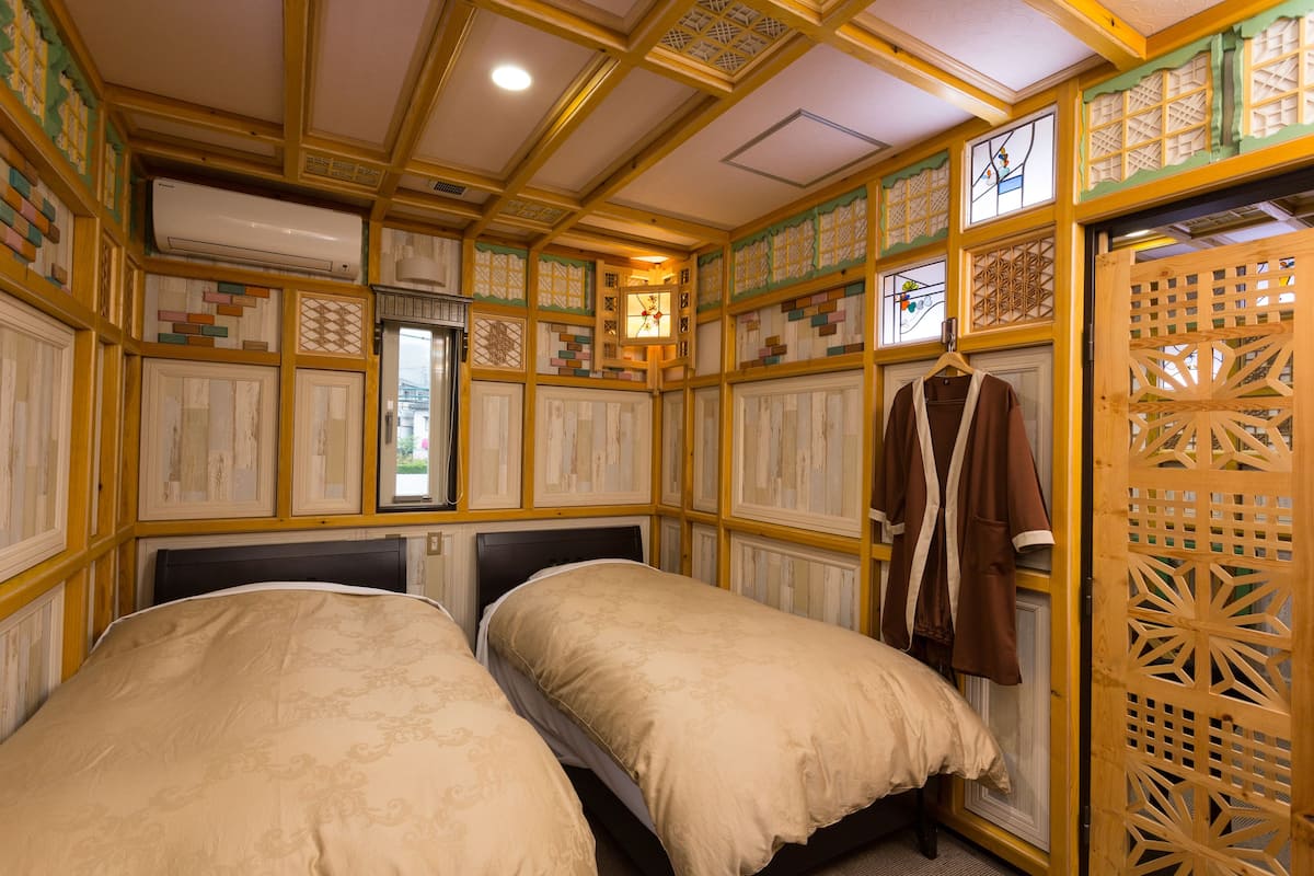 A traditional Japanese-style room with two beds, wooden paneling, and a hanging robe.