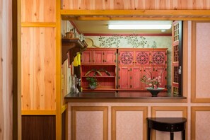 A kitchen with wooden cabinets, a countertop, and a black stool. - At Inn (Yufu)
