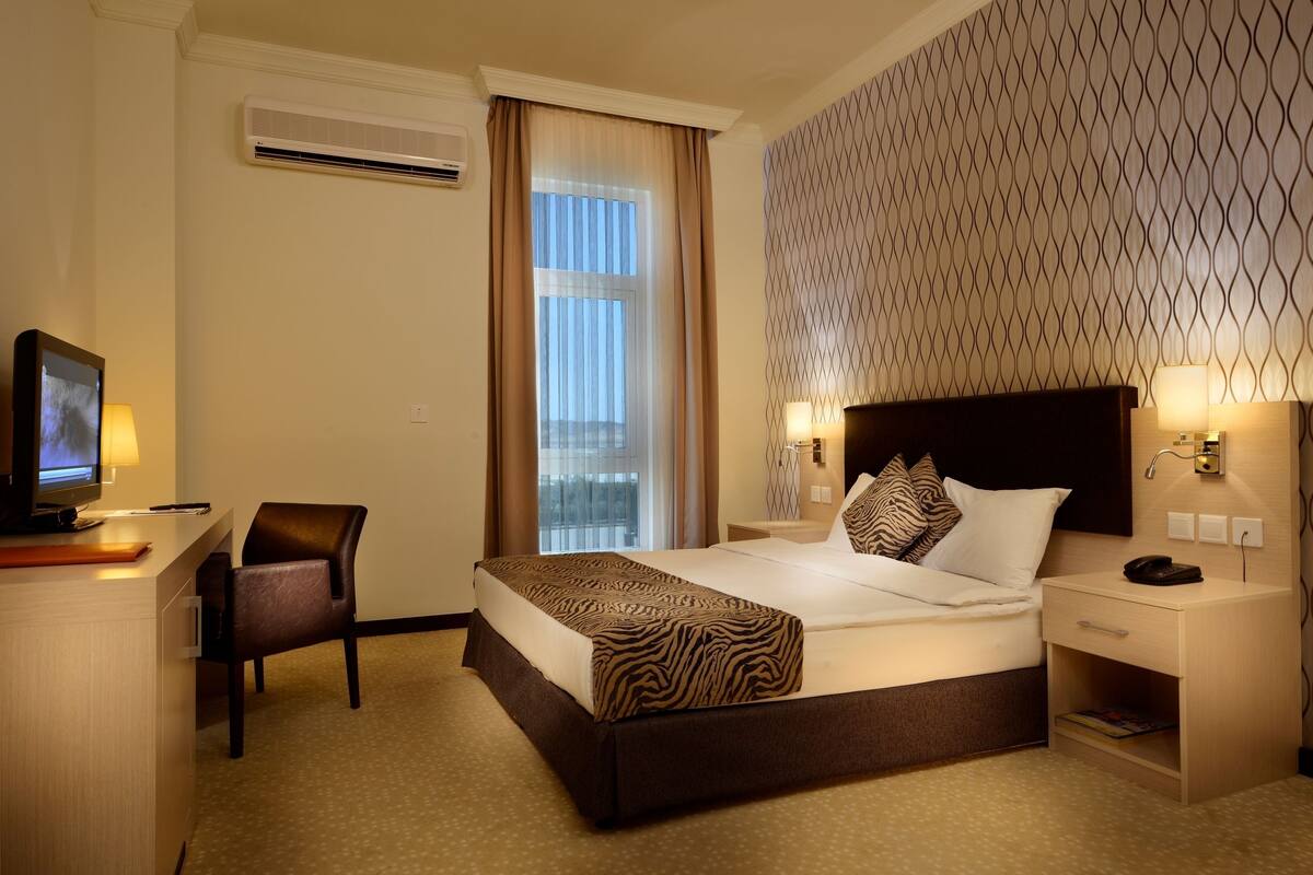 Una habitación de hotel con cama, escritorio con silla, televisión y pared con diseño.