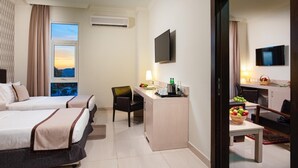 Une chambre d’hôtel avec deux lits, un bureau, une chaise, une télévision et une vue sur le coucher de soleil par la fenêtre.
