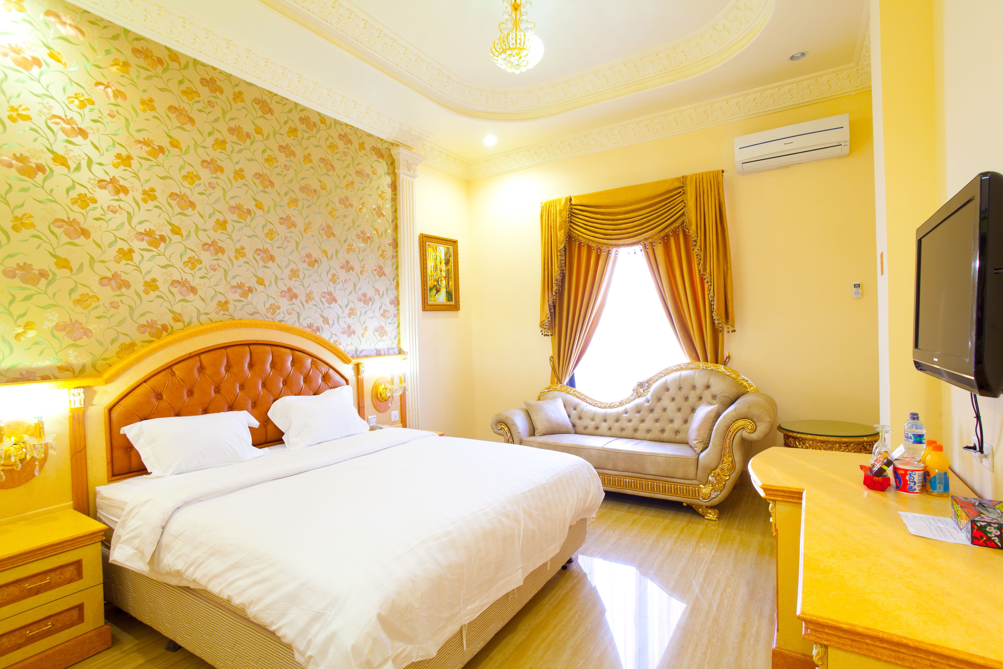 A hotel room with a large bed, a sofa, a television, and a desk with a bottle and a cup.