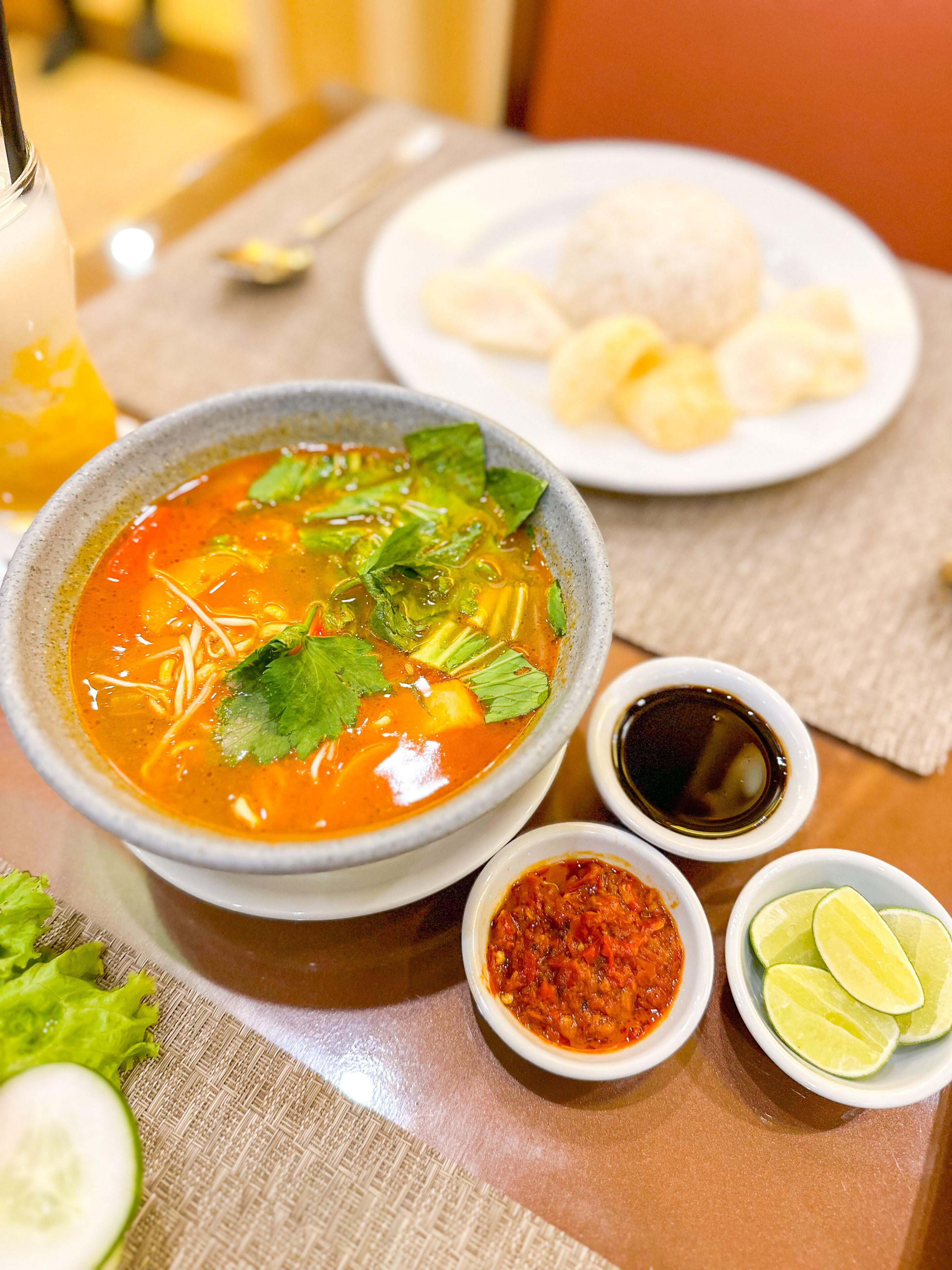 A bowl of soup with lime wedges and a small bowl of sauce on a table.