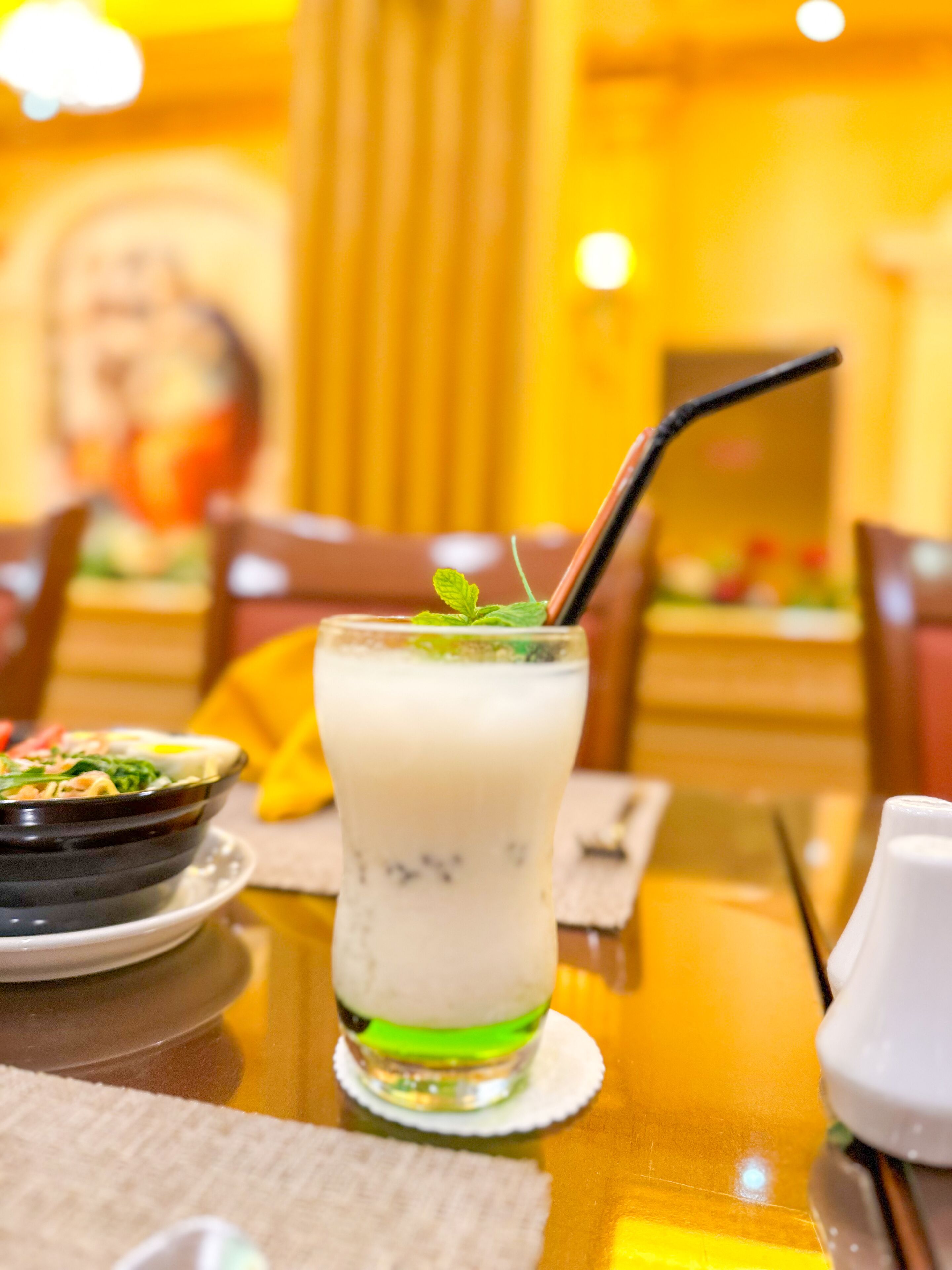 A glass of a creamy beverage with a straw and mint garnish on a table in a restaurant.