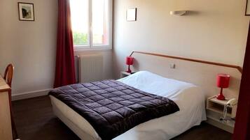 Un lit bien fait, recouvert d’une couverture sombre, une lampe rouge sur chaque table de chevet et une fenêtre ornée de rideaux rouges.