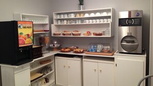 A kitchenette with a coffee machine, shelves with cups and bowls, and a refrigerator with a fruit display. - Hotel Le Saint Remy (Saint-Remy)