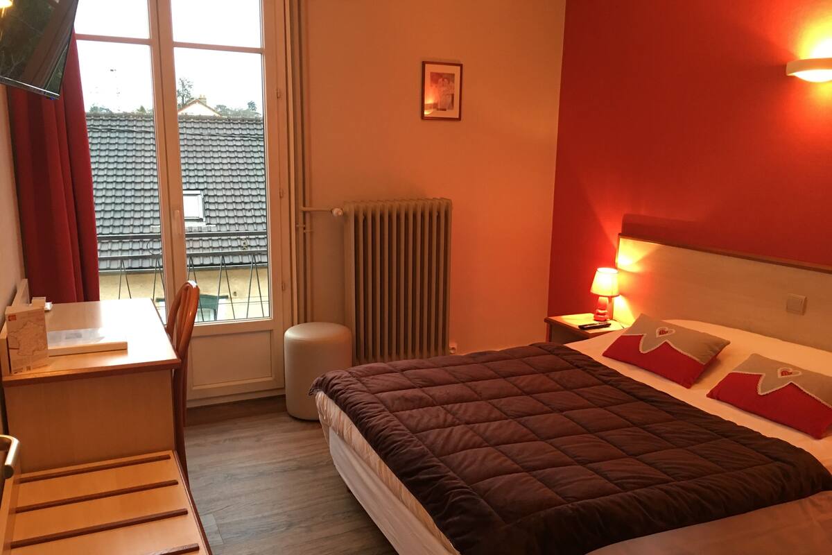 Ein Hotelzimmer mit Bett, Schreibtisch, Stuhl, Heizkörper und einem Fenster mit Vorhängen.