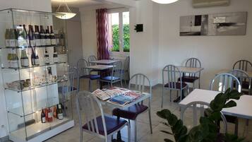 A dining area with tables and chairs, a wine display, and a view of greenery outside.