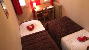 Une chambre avec deux lits, chacun agrémenté d’un oreiller en forme de cœur, un bureau avec une lampe et un radiateur.