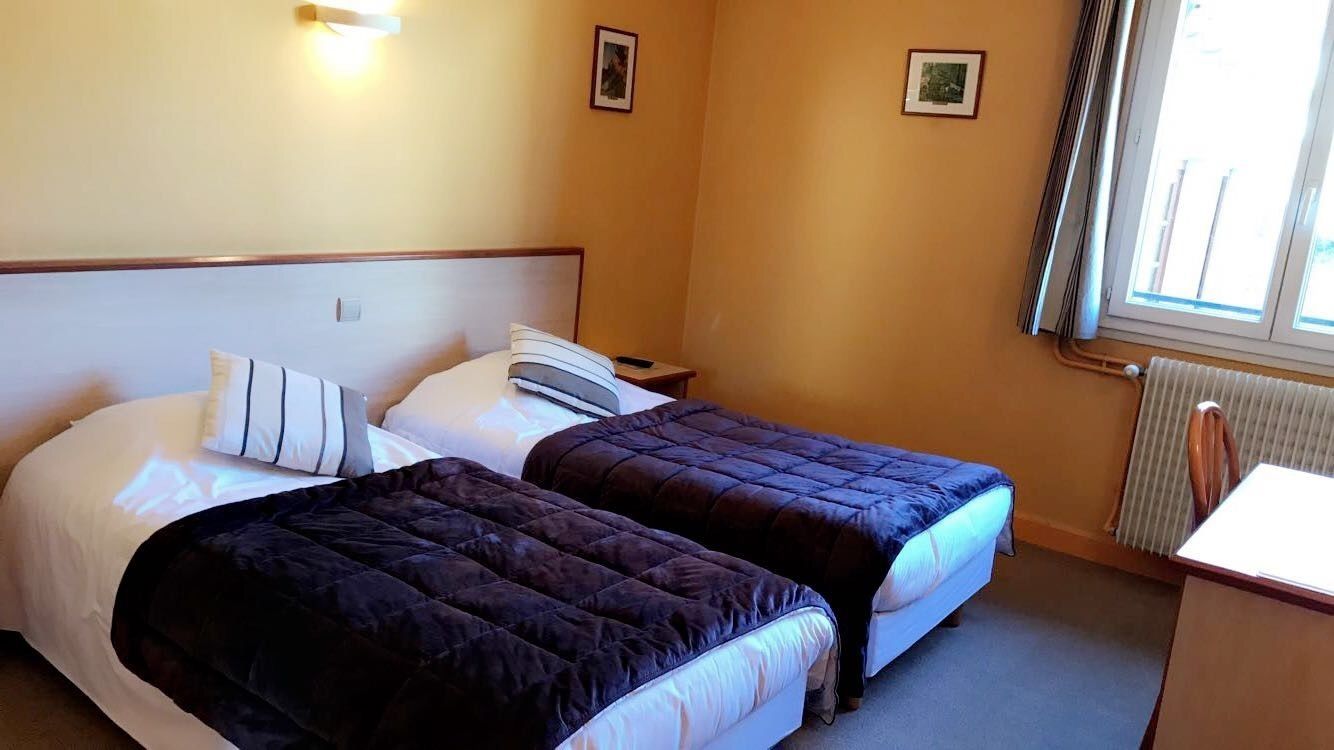 Habitación de hotel con dos camas, una mesita de noche, un escritorio y una ventana con cortinas.