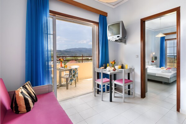 A hotel room with a balcony, a dining area, and a bed. - Louladakis Apartments (Platanias)
