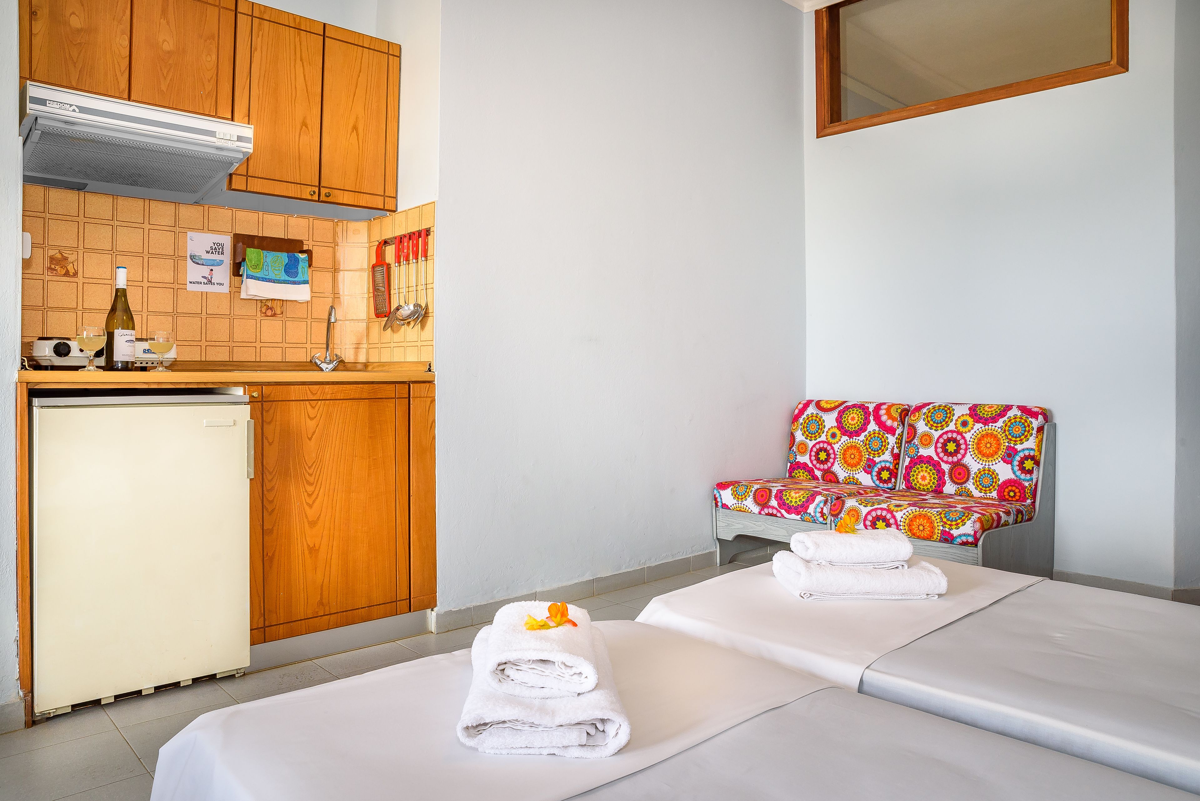 A room with a kitchenette, a bed with towels, and a colorful chair.