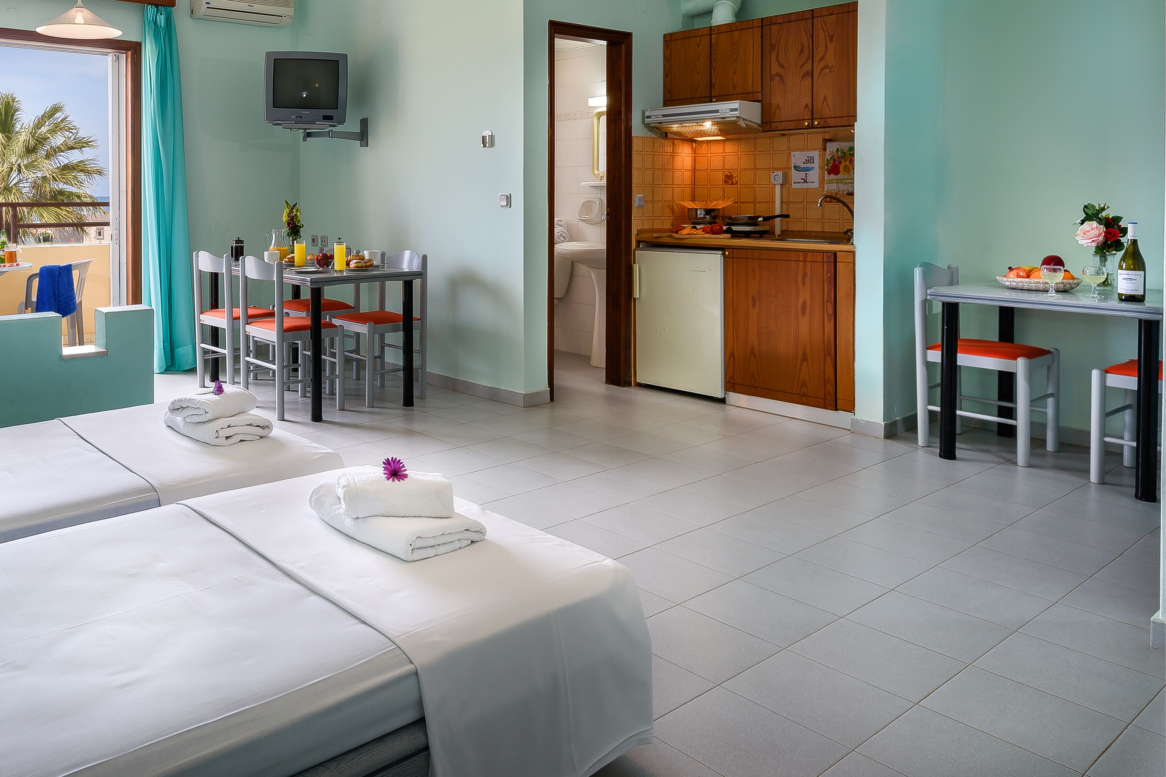A hotel room with two beds, a dining area, a kitchen, and a bathroom.