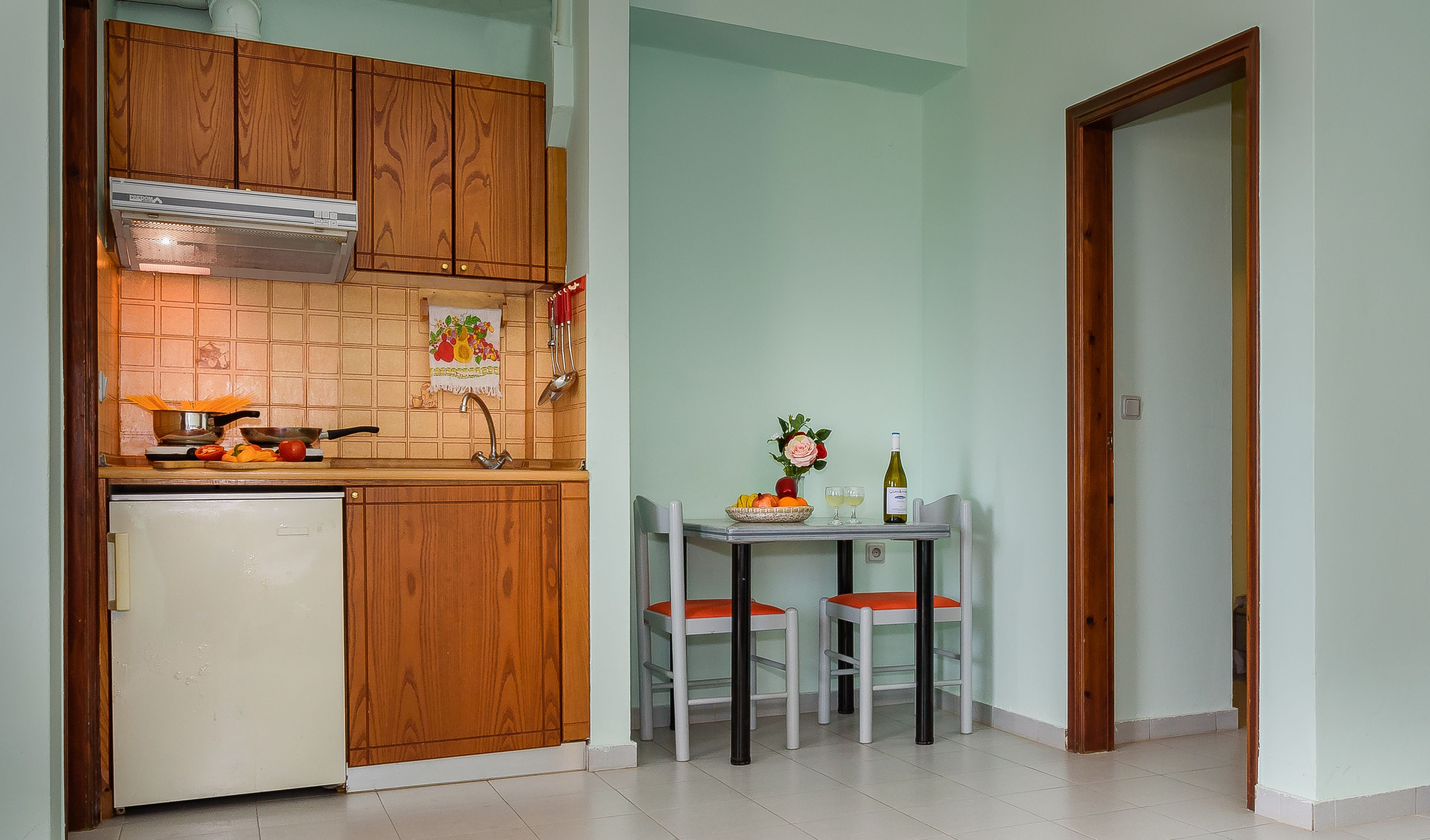 A compact kitchen with wooden cabinets, a built-in oven, and a small dining table with two chairs.