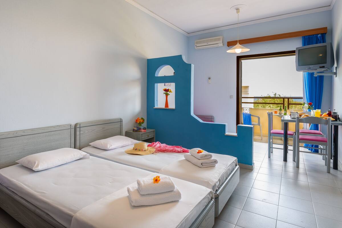 A hotel room with two beds, a TV, and a balcony with breakfast items.